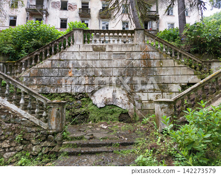 Abandoned stone staircase overgrown with green vegetation in city of Akarmara, Abkhazia. Grand symmetrical steps of a ruined building covered in moss. Historical architecture Abandoned stone staircase overgrown with green vegetation in city of Akarmara, Abkhazia. Grand symmetrical steps of a ruined building covered in moss. Historical architecture 142273579