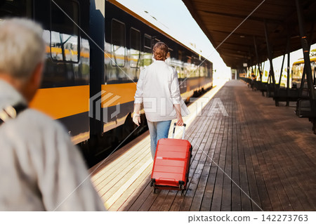 passenger with luggage is walking on the train station platform for departure. The man pulls a red suitcase to start his travel journey. passenger with luggage is walking on the train station platform for departure. The man pulls a red suitcase to start his travel journey. 142273763
