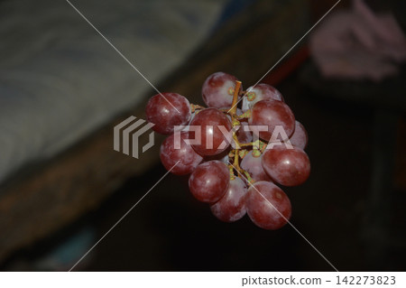 Bunch of fresh red grapes hanging against a dark background with still life Bunch of fresh red grapes hanging against a dark background with still life 142273823
