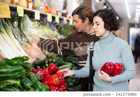 Couple man and woman choosing peppers in vegetable shop Couple man and woman choosing peppers in vegetable shop 142273960