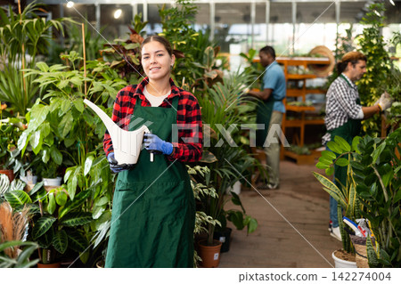 Smiling salesgirl posing among ornamental plants in gardening store Smiling salesgirl posing among ornamental plants in gardening store 142274004