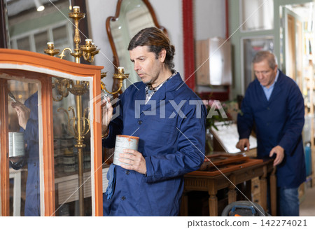 Professional furniture male restorer renewing vintage chest of drawers in workshop 142274021