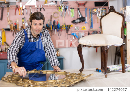 Portrait of middle-aged skillful repairman carpenter renovating chair furniture using tools in woodwork studio Portrait of middle-aged skillful repairman carpenter renovating chair furniture using tools in woodwork studio 142274057