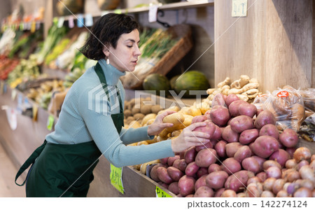 Woman shop seller puts potato goods on display case Woman shop seller puts potato goods on display case 142274124