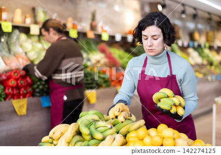 Adult woman seller puts bananas on display Adult woman seller puts bananas on display 142274125