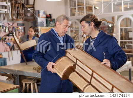 Two male restorers inspecting vintage chest of drawers before restoration in restoration workshop Two male restorers inspecting vintage chest of drawers before restoration in restoration workshop 142274134