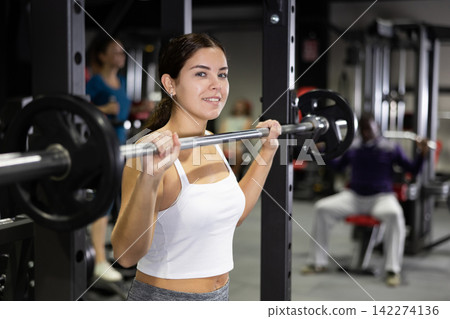 Caucasian woman training with barbell using squat rack in gym Caucasian woman training with barbell using squat rack in gym 142274136