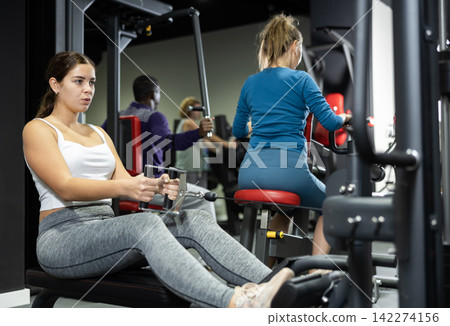 Woman is engaged in a simulator with horizontal weights in gym Woman is engaged in a simulator with horizontal weights in gym 142274156
