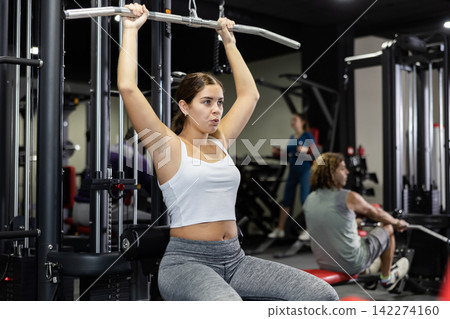 Caucasian woman doing exercises on lat pull down machine in gym Caucasian woman doing exercises on lat pull down machine in gym 142274160