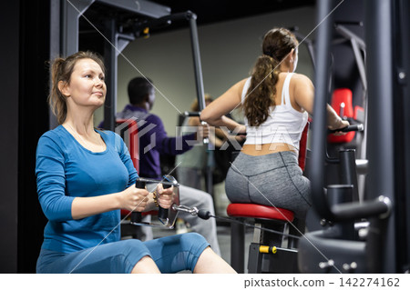 Caucasian woman doing exercises on cable row machine in gym Caucasian woman doing exercises on cable row machine in gym 142274162