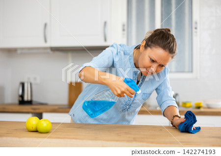 Focused woman cleaning kitchen table at home Focused woman cleaning kitchen table at home 142274193