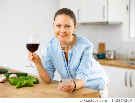 Woman searching for recipes online and holding a glass of wine in the kitchen Woman searching for recipes online and holding a glass of wine in the kitchen 142274209