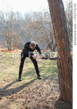 Young man using resistance band for strength training in forest Young man using resistance band for strength training in forest 142274230