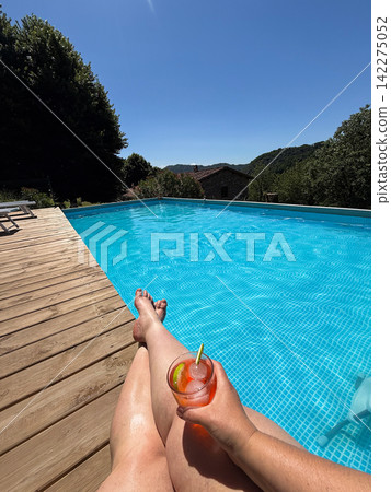 Person relaxing by pool drinking cocktail on vacation Person relaxing by pool drinking cocktail on vacation 142275052