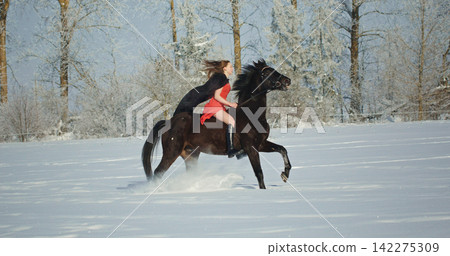 Woman riding a galloping horse through winter snow 142275309