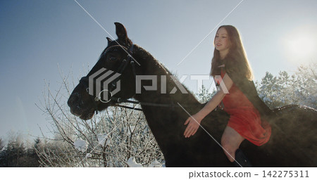 Woman riding horse in winter wonderland with red dress Woman riding horse in winter wonderland with red dress 142275311