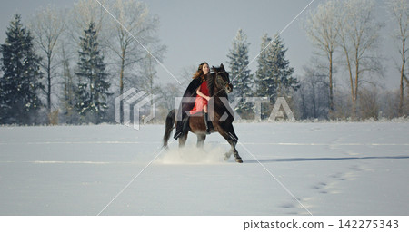 Woman riding horse in snow wearing red dress Woman riding horse in snow wearing red dress 142275343