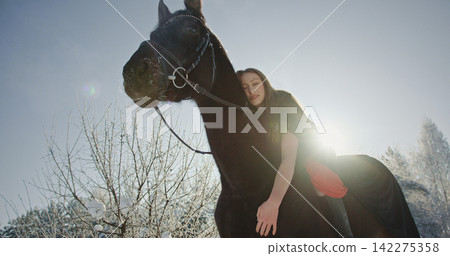 Young woman enjoying warm sunshine with horse in winter 142275358