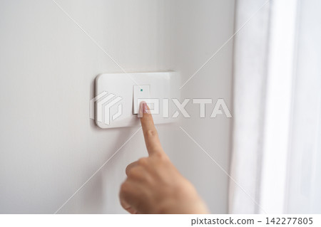 Female finger pushing for turn on light switch on white wall at home room. Woman hand turn off lighting Switch. Energy Saving, energy power control, electrical, eco environment, and lifestyle concept Female finger pushing for turn on light switch on white wall at home room. Woman hand turn off lighting Switch. Energy Saving, energy power control, electrical, eco environment, and lifestyle concept 142277805