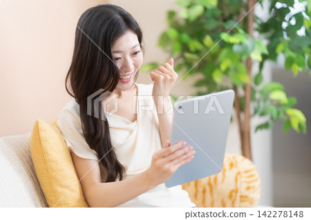 一位年輕女子看著她的平板電腦,欣喜若狂(擺出勝利的姿勢)。 一位年輕女子看著她的平板電腦,欣喜若狂(擺出勝利的姿勢)。 142278148