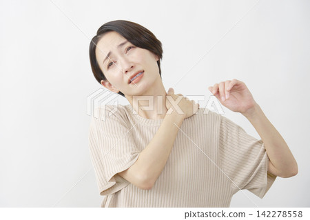 A woman in her 40s suffering from stiff shoulders against a white background. A woman in her 40s suffering from stiff shoulders against a white background. 142278558