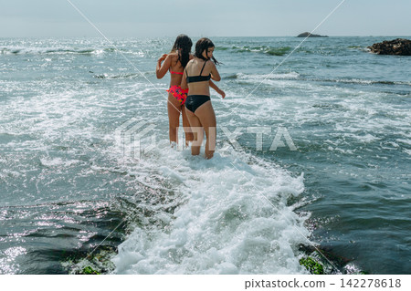 Two Girls Wading Into Ocean Waves on a Sunny Summer Day Two Girls Wading Into Ocean Waves on a Sunny Summer Day 142278618