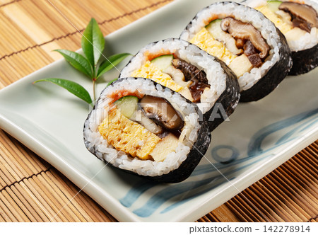 A thick sushi roll on a Japanese plate placed on a bamboo mat; a beautifully cross-sectioned rolled sushi, Ehomaki. A thick sushi roll on a Japanese plate placed on a bamboo mat; a beautifully cross-sectioned rolled sushi, Ehomaki. 142278914