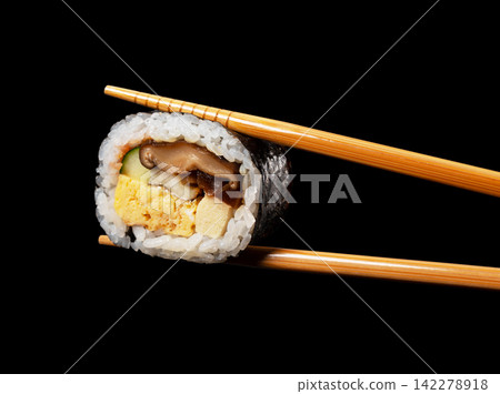 A cross-section of a single slice of futomaki (thick sushi roll) being picked up with chopsticks, isolated against a black background. (Chopstick lift, cutout material) A cross-section of a single slice of futomaki (thick sushi roll) being picked up with chopsticks, isolated against a black background. (Chopstick lift, cutout material) 142278918