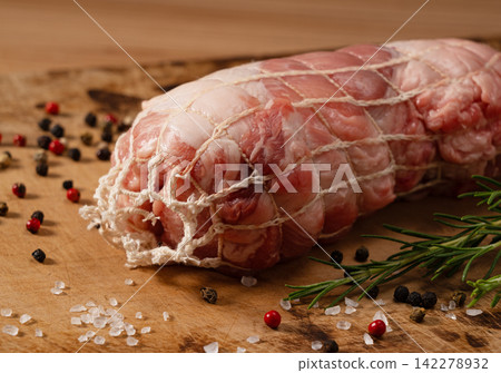 用網袋包裹的生豬肉塊放在木製砧板上,拍攝了一張微距照片,捕捉了它的質感和吸引力。 用網袋包裹的生豬肉塊放在木製砧板上,拍攝了一張微距照片,捕捉了它的質感和吸引力。 142278932