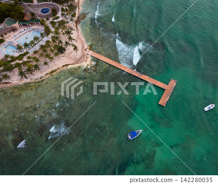 Aerial view of sandy beach with wooden pier leading over the Caribbean sea Aerial view of sandy beach with wooden pier leading over the Caribbean sea 142280035
