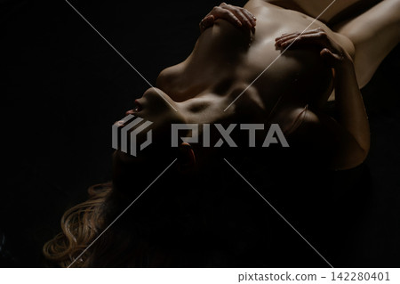 Woman lying back with hands on chest under dramatic lighting Woman lying back with hands on chest under dramatic lighting 142280401