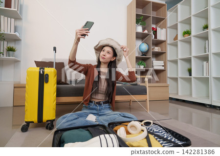 Asian woman taking selfie while packing luggage for travel vacation Asian woman taking selfie while packing luggage for travel vacation 142281386
