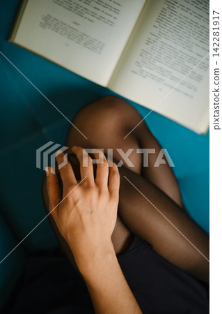 Reading a book while sitting on a blue surface with bare hand resting on black tights Reading a book while sitting on a blue surface with bare hand resting on black tights 142281917