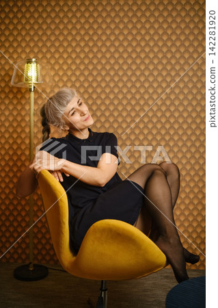 Woman sitting in a yellow chair inside a room with decorative wall and lamp Woman sitting in a yellow chair inside a room with decorative wall and lamp 142281920