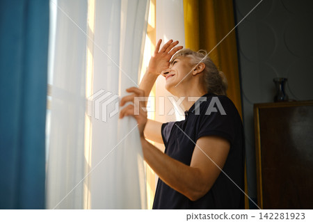 Person looking out window while holding curtains in bright indoor space during daylight hours Person looking out window while holding curtains in bright indoor space during daylight hours 142281923