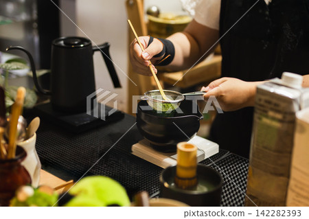Barista sifting matcha powder using a traditional bamboo scoop. Barista sifting matcha powder using a traditional bamboo scoop. 142282393