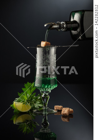 Absinthe is poured from an vintage bottle into a glass. Absinthe is poured from an vintage bottle into a glass. 142282812
