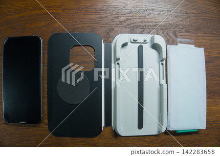 Smartphone beside a tempered glass screen protector installation kit, flat lay Smartphone beside a tempered glass screen protector installation kit, flat lay 142283658