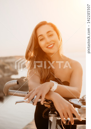 Woman bicycle sunset smiling young woman leaning on her bike handlebar during golden hour by the ocean coast for wellness Woman bicycle sunset smiling young woman leaning on her bike handlebar during golden hour by the ocean coast for wellness 142285507