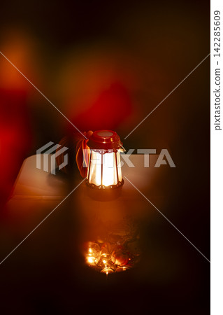 Glowing red metal lantern and decorative candles illuminate in a warm dark environment, illustrating a cozy autumn evening spirit. Glowing red metal lantern and decorative candles illuminate in a warm dark environment, illustrating a cozy autumn evening spirit. 142285609