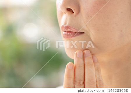 A woman touches her cheek, troubled. A woman touches her cheek, troubled. 142285668