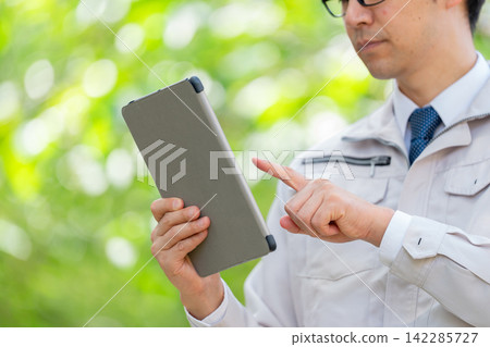 一名身穿工作服的男子手持平板電腦（雙手） 142285727