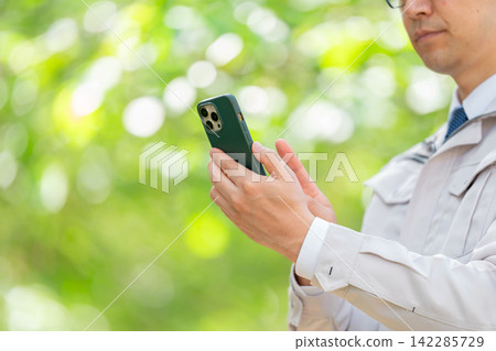 A man in work clothes holding a smartphone (hands) A man in work clothes holding a smartphone (hands) 142285729
