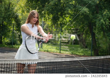 Female tennis player hitting forehand near net outdoors Female tennis player hitting forehand near net outdoors 142285843