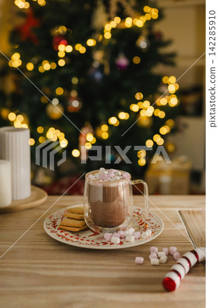 Holiday, Christmas background. A cup with hot chocolate and marshmallows on the table with Christmas tree on background 142285910