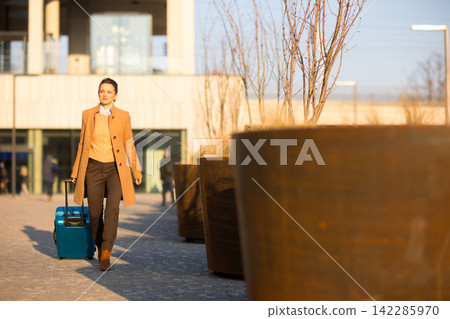 Confident Woman Pulling Blue Suitcase near Modern Station Confident Woman Pulling Blue Suitcase near Modern Station 142285970