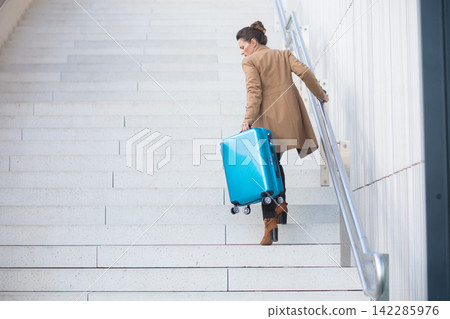 Traveler Pulling Blue Suitcase Up Modern Stairs Traveler Pulling Blue Suitcase Up Modern Stairs 142285976