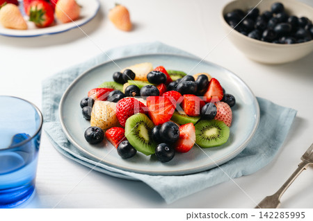 Fresh fruit salad in a plate, kiwi slices, strawberries and blueberries. Healthy food, sweet dessert, top view Fresh fruit salad in a plate, kiwi slices, strawberries and blueberries. Healthy food, sweet dessert, top view 142285995