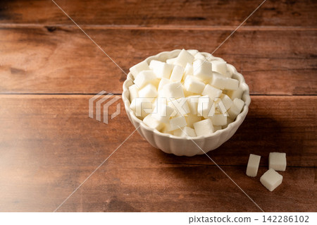 White sugar cubes in a white bowl on wooden background. White sugar cubes in a white bowl on wooden background. 142286102