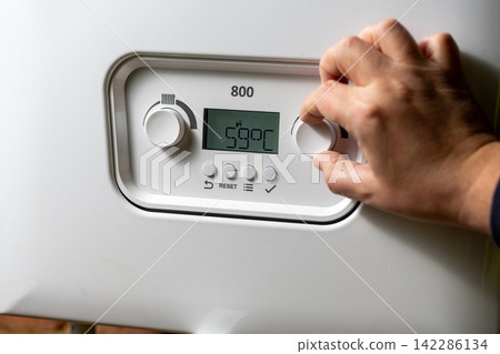 Men hand setting temperature button on control panel of central heating at combi boiler. Incressing price for gas Men hand setting temperature button on control panel of central heating at combi boiler. Incressing price for gas 142286134